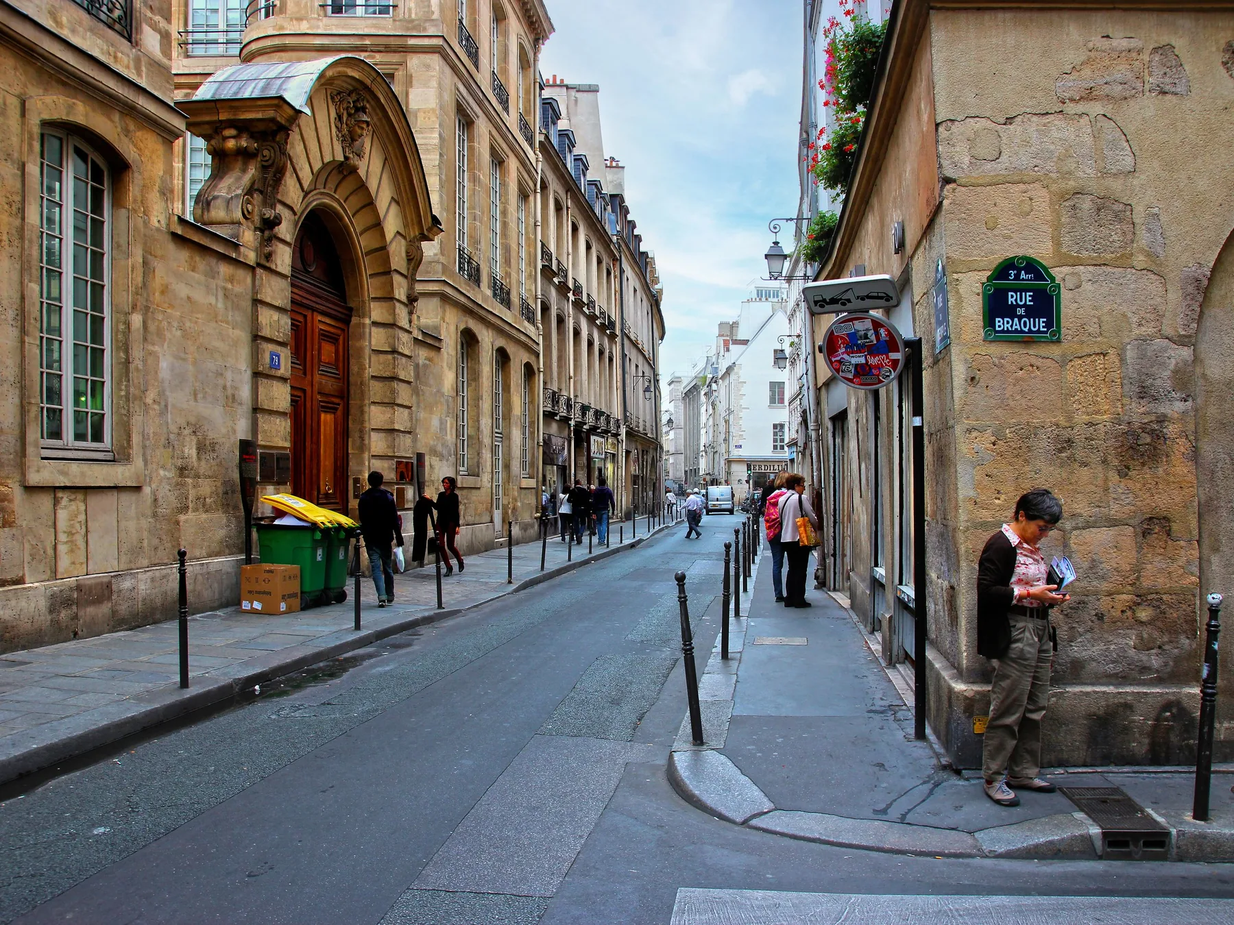 A narrow Marais street of honey-coloured stone townhouses beneath a blue sky, with a street-name plate on the corner